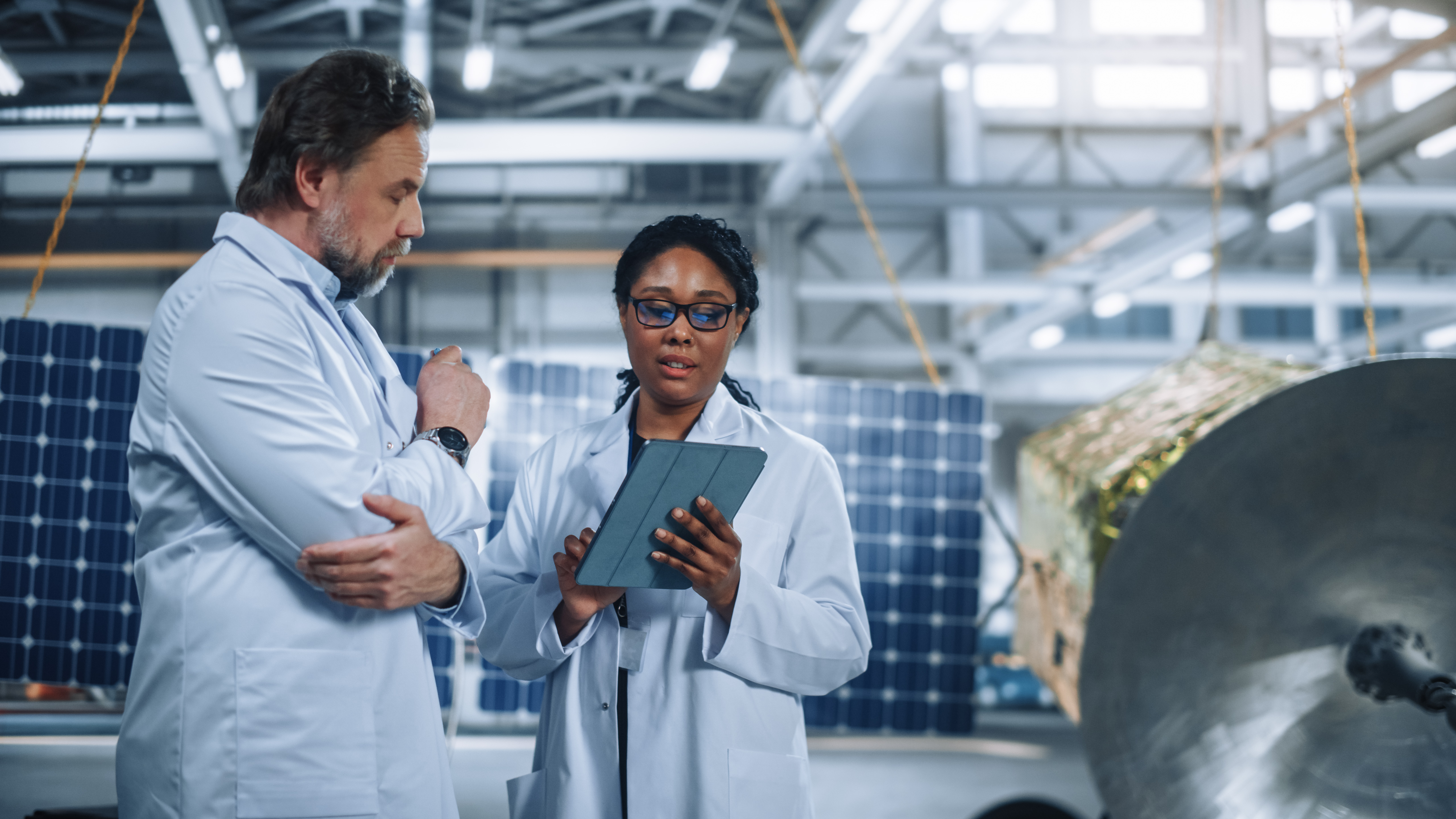 Two,Engineers,Talk,,Use,Tablet,Computer,While,Working,On,Satellite